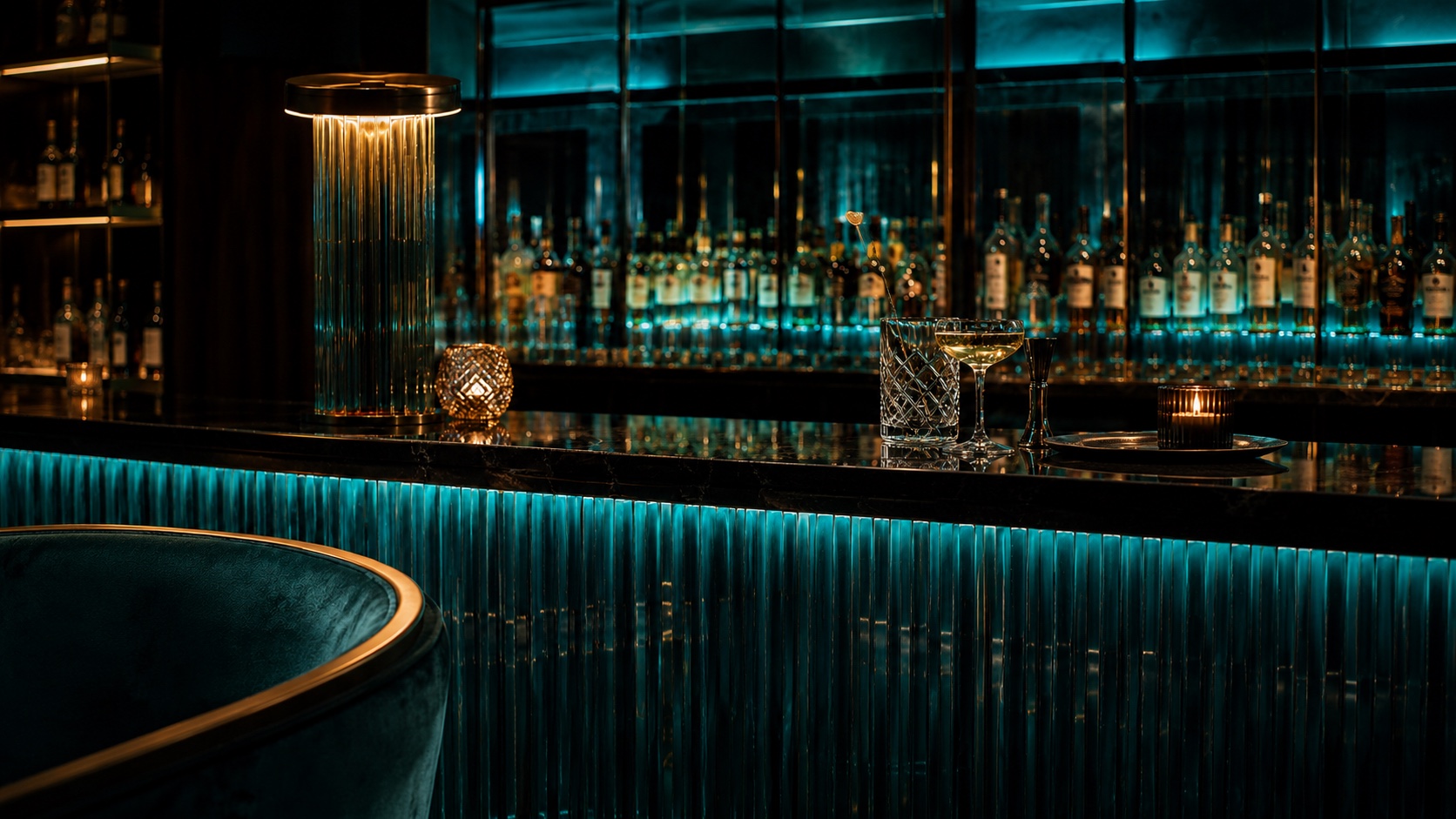 The Qï bar with backlit spirits behind a teal ribbed-glass bar front