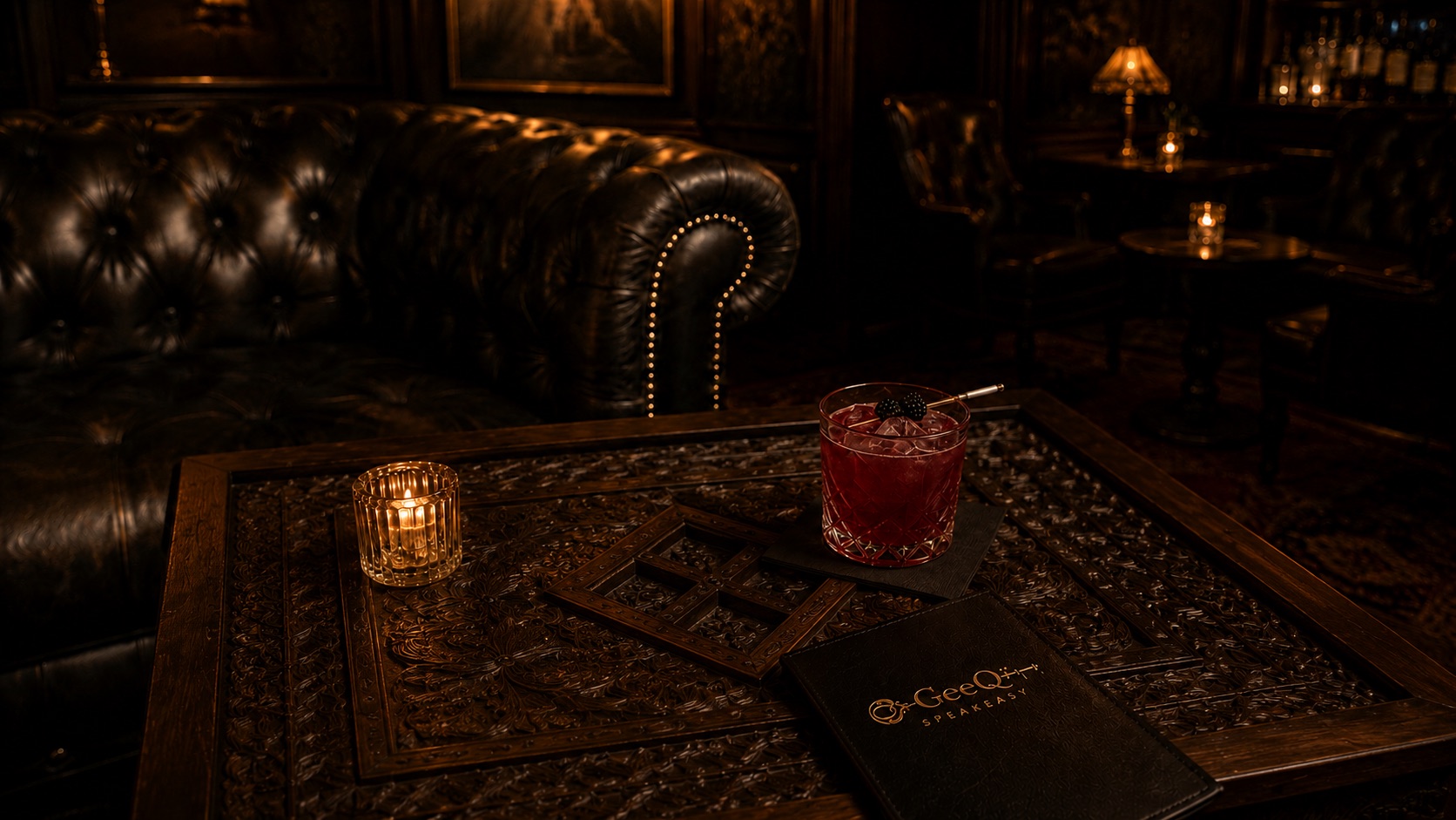 A red cocktail with a blackberry garnish on a carved wood table beside a votive and a black GeeQï Speakeasy menu, before a tufted leather chesterfield